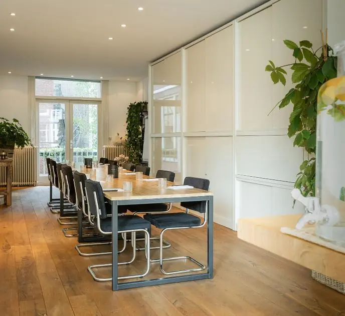 Vergaderruimte aan de Van Baerlestraat met lange tafel, moderne stoelen en veel groen.